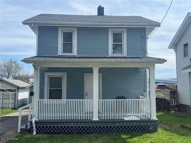 view of front facade with a front yard, a porch, a chimney, and a shingled roof