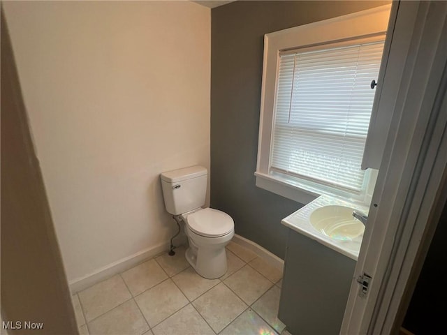 half bath with toilet, vanity, baseboards, and tile patterned flooring