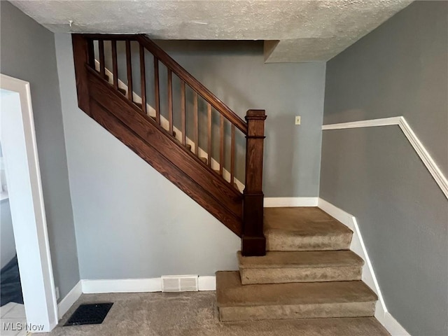 staircase with a textured ceiling, carpet flooring, baseboards, and visible vents