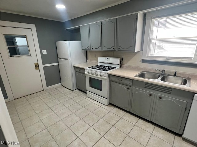 kitchen with a sink, gray cabinets, light countertops, and white appliances