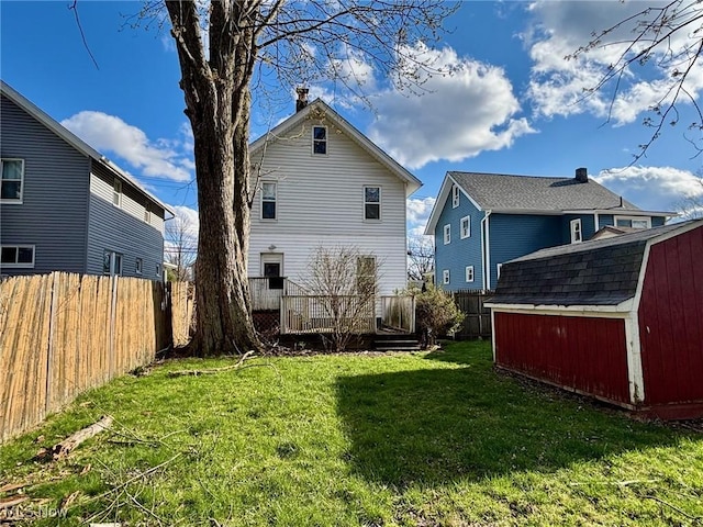 back of property with an outbuilding, a shed, a wooden deck, a fenced backyard, and a lawn