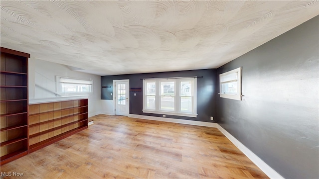 spare room with light wood-type flooring, baseboards, and a textured ceiling