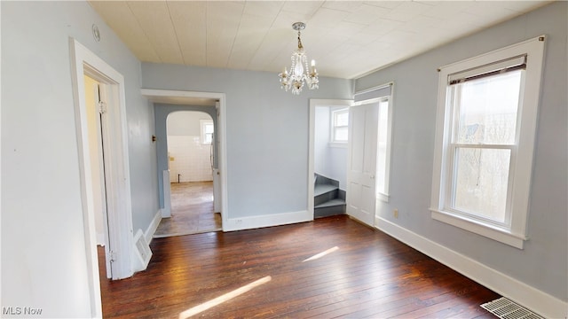 unfurnished dining area with an inviting chandelier, arched walkways, visible vents, hardwood / wood-style floors, and baseboards
