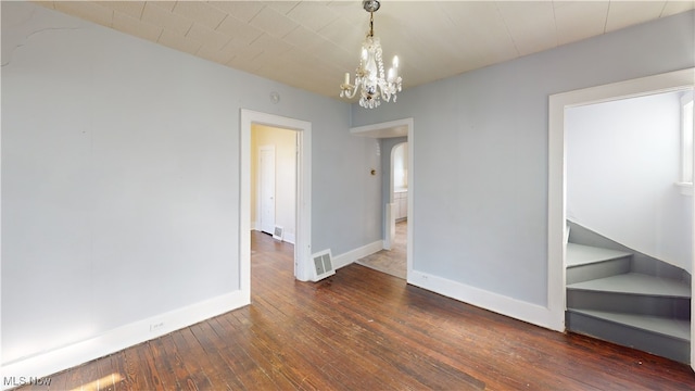 spare room with a notable chandelier, baseboards, visible vents, arched walkways, and hardwood / wood-style flooring