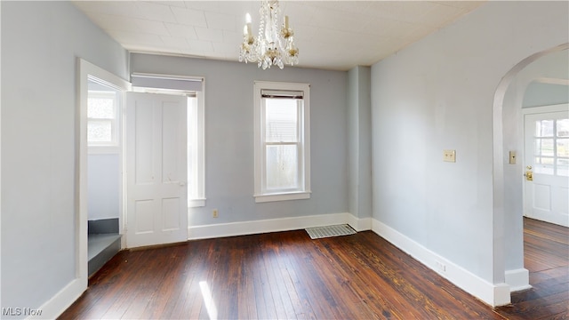 empty room with a notable chandelier, baseboards, visible vents, arched walkways, and wood-type flooring