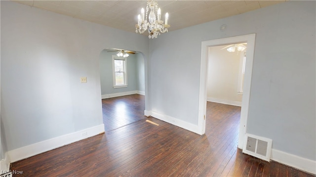 spare room featuring ceiling fan with notable chandelier, arched walkways, visible vents, hardwood / wood-style floors, and baseboards