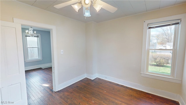 empty room with ceiling fan with notable chandelier, baseboards, plenty of natural light, and dark wood finished floors