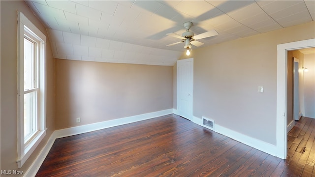 empty room featuring baseboards, plenty of natural light, dark wood-style floors, a ceiling fan, and visible vents