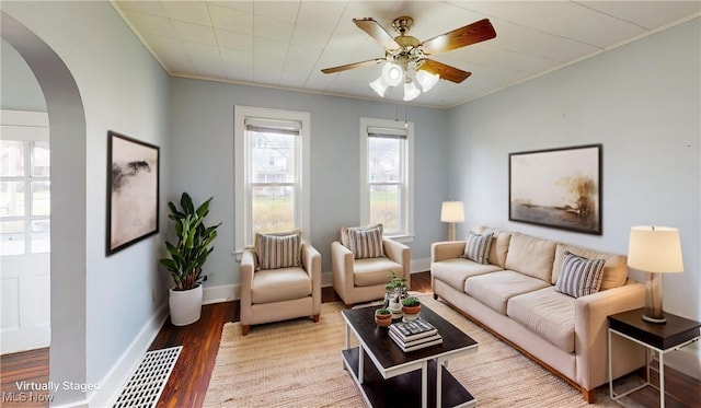 living room featuring arched walkways, ornamental molding, a ceiling fan, wood finished floors, and baseboards
