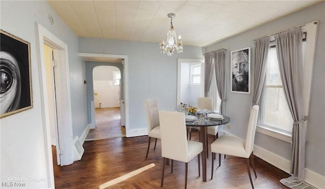 dining room featuring parquet floors, arched walkways, a notable chandelier, and baseboards
