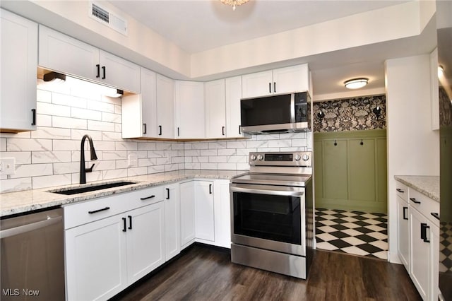 kitchen featuring white cabinets, stainless steel appliances, a sink, visible vents, and light stone counters