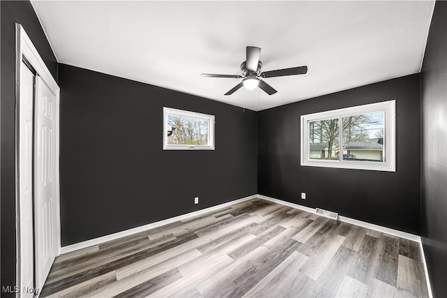 unfurnished bedroom with a closet, baseboards, a ceiling fan, visible vents, and wood finished floors