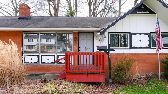 doorway to property with a chimney, a shingled roof, and brick siding