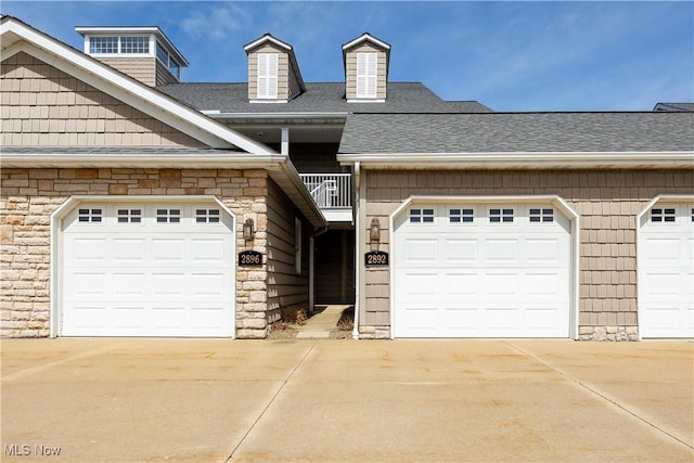 view of front of house featuring stone siding, concrete driveway, and a shingled roof