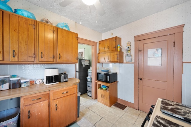 14117 Sylvia Ave, Cleveland, OH 44110 - kitchen with brown cabinetry, wallpapered walls, freestanding refrigerator, and black microwave