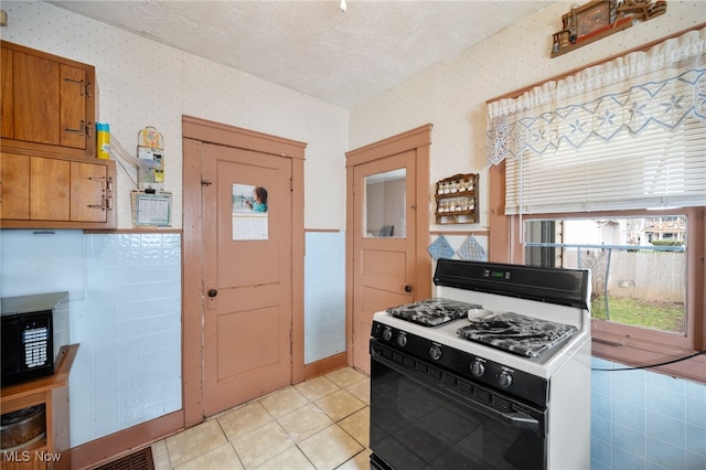 14117 Sylvia Ave, Cleveland, OH 44110 - kitchen with range with gas cooktop, light tile patterned floors, a textured ceiling, brown cabinets, and wallpapered walls