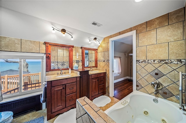 bathroom featuring a whirlpool tub, two vanities, healthy amount of natural light, tile walls, and lofted ceiling
