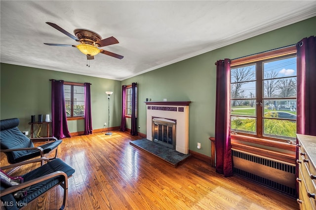 living area with healthy amount of natural light, baseboards, wood finished floors, a ceiling fan, and ornamental molding