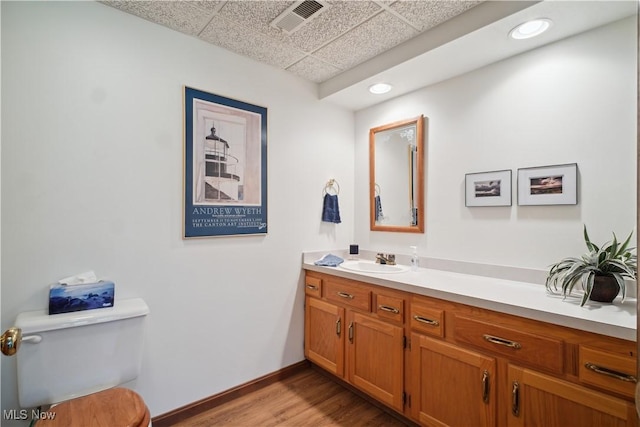 bathroom featuring visible vents, toilet, vanity, wood finished floors, and a drop ceiling
