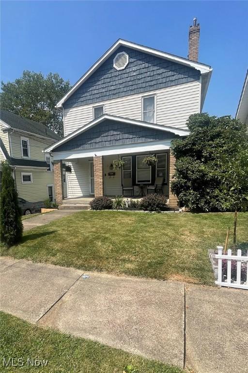 view of front of home featuring brick siding, a chimney, a front lawn, and a porch