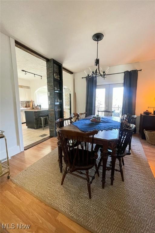 dining space featuring arched walkways, wood finished floors, an inviting chandelier, and rail lighting
