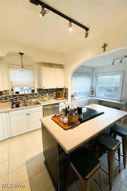 kitchen with light countertops, white cabinetry, decorative backsplash, stainless steel dishwasher, and a sink