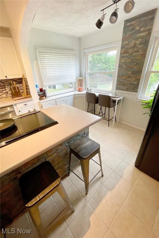 kitchen featuring a wainscoted wall, white cabinetry, light tile patterned flooring, and black electric cooktop