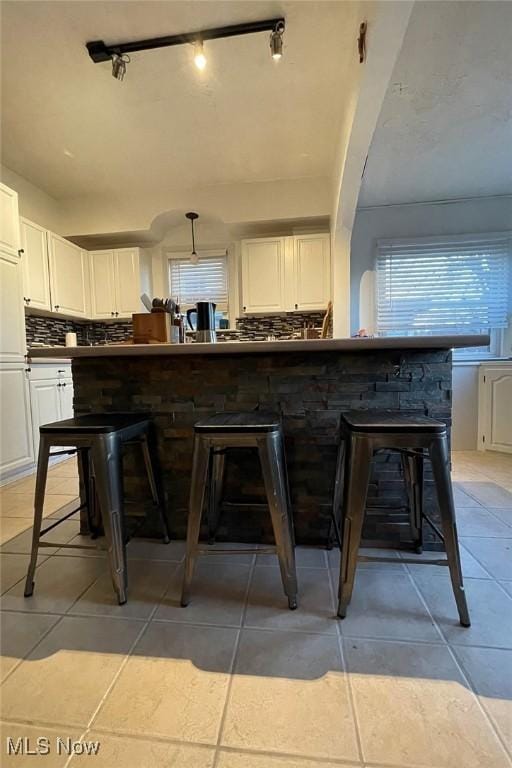 kitchen with tasteful backsplash, a breakfast bar, light tile patterned floors, white cabinetry, and dark countertops