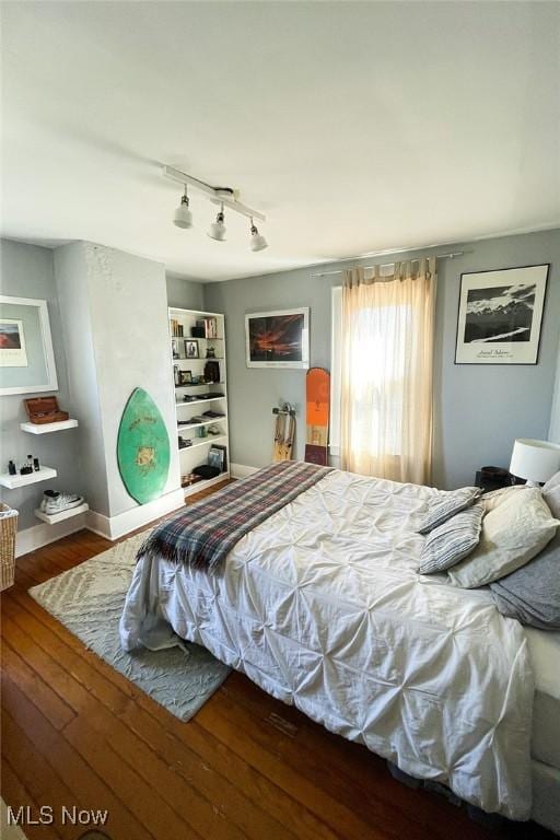 bedroom featuring track lighting, wood finished floors, and baseboards