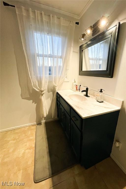 bathroom featuring vanity, baseboards, ornamental molding, and a healthy amount of sunlight