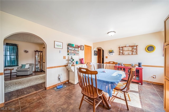 2457 Sheffield Rd, Jefferson, OH 44047 - dining space featuring arched walkways, wainscoting, baseboard heating, tile patterned floors, and wooden walls