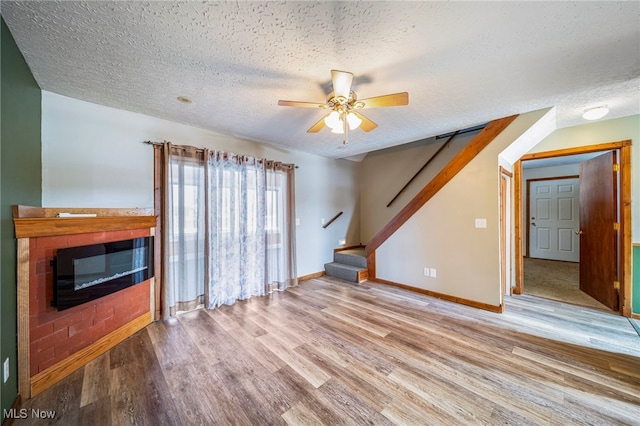 2457 Sheffield Rd, Jefferson, OH 44047 - unfurnished living room featuring a textured ceiling, wood finished floors, ceiling fan, stairs, and a glass covered fireplace