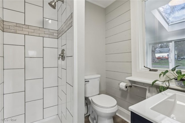bathroom with a tile shower, vanity, toilet, a skylight, and wooden walls