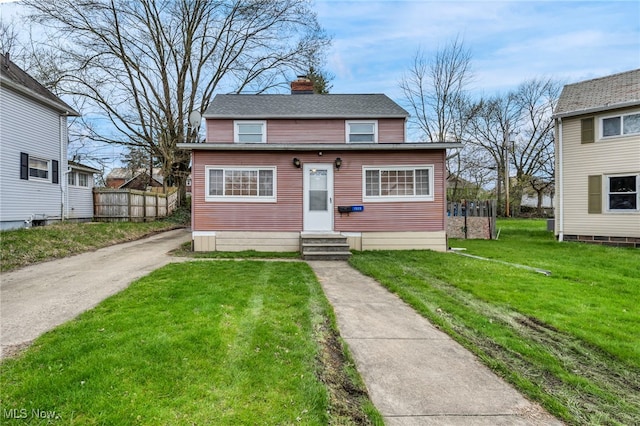 bungalow-style house with entry steps, a front lawn, fence, and a chimney