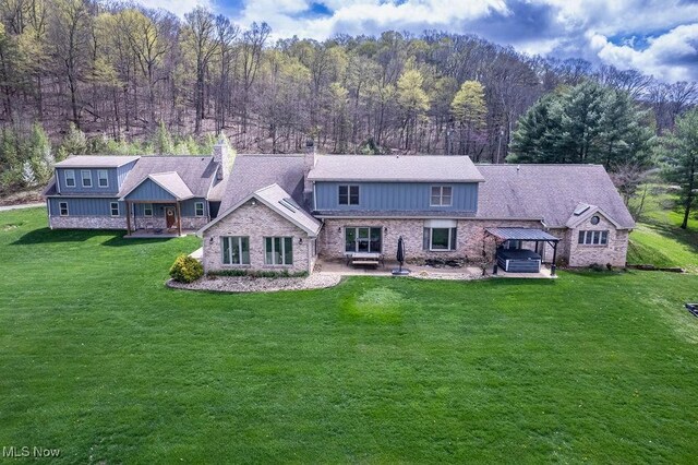 rear view of property with a yard, a forest view, and a chimney