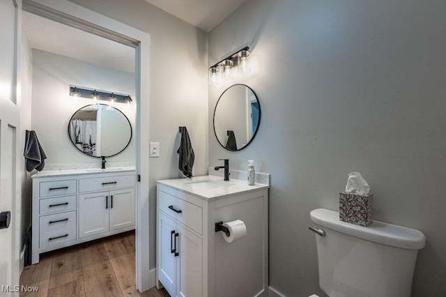 bathroom featuring a sink, two vanities, wood finished floors, and toilet