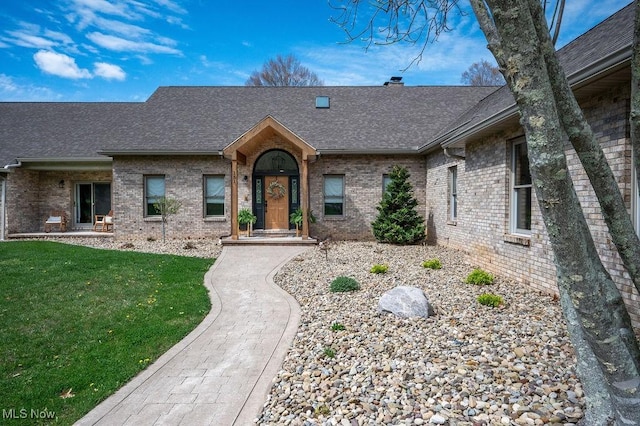view of front of property featuring a shingled roof, a front yard, and brick siding