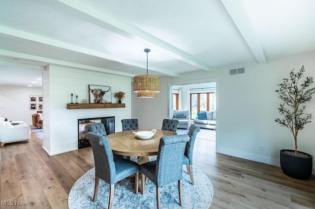 dining space featuring beamed ceiling, a glass covered fireplace, visible vents, wood finished floors, and baseboards