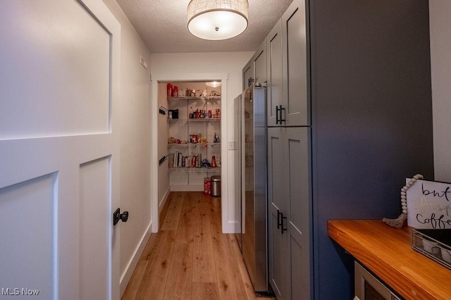 hall with light wood-style floors, a textured ceiling, and baseboards