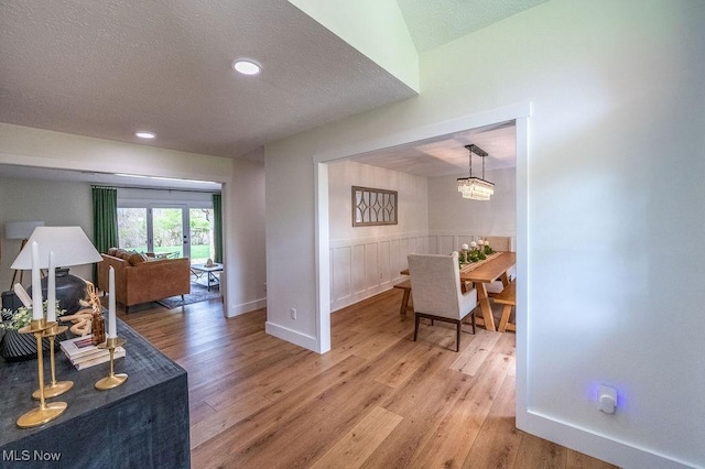 interior space featuring light wood-type flooring, a textured ceiling, recessed lighting, a wainscoted wall, and baseboards