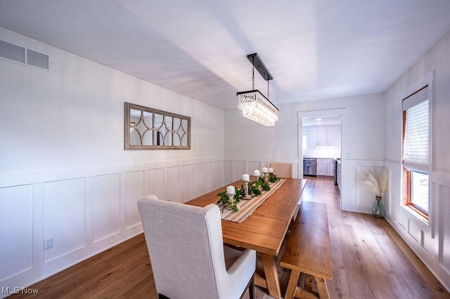 dining room featuring wood finished floors, an inviting chandelier, wainscoting, and visible vents