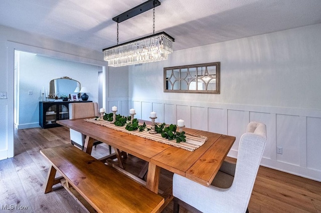 dining room with an inviting chandelier, a wainscoted wall, and wood finished floors