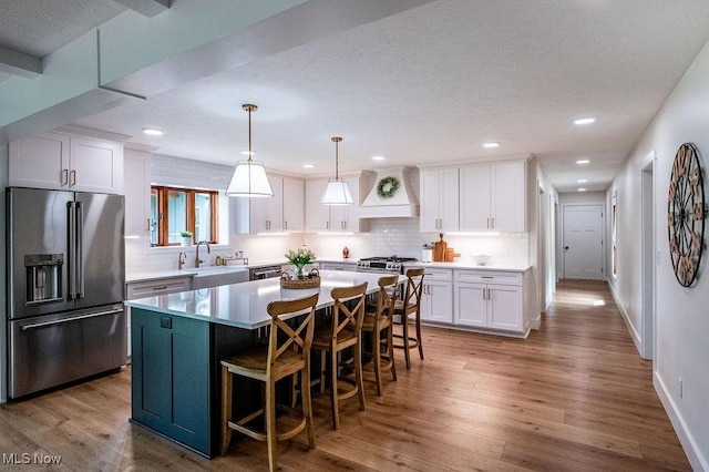 kitchen with custom range hood, white cabinetry, high end fridge, and wood finished floors