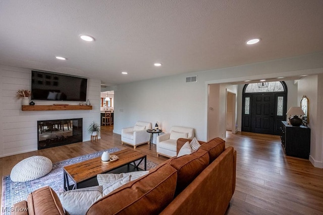living area featuring recessed lighting, a textured ceiling, a multi sided fireplace, visible vents, and hardwood / wood-style flooring
