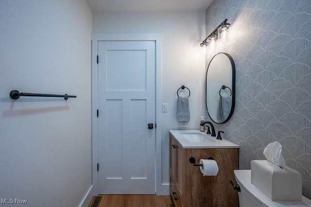 half bath with vanity, visible vents, toilet, and wood finished floors