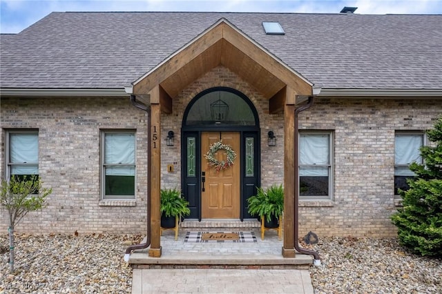 doorway to property with brick siding and a shingled roof