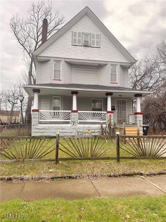 american foursquare style home with a chimney, covered porch, and a fenced front yard