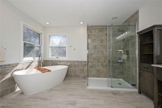 full bathroom featuring a shower stall, a soaking tub, wainscoting, and tile walls
