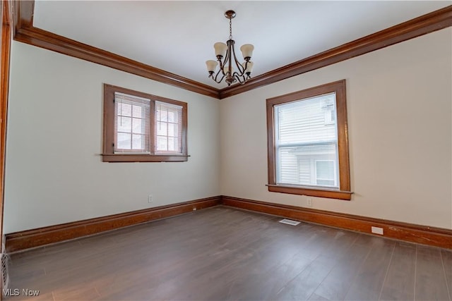 empty room with crown molding, visible vents, a chandelier, wood finished floors, and baseboards