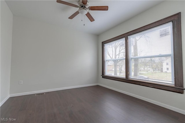 empty room featuring dark wood-type flooring, visible vents, baseboards, and a ceiling fan